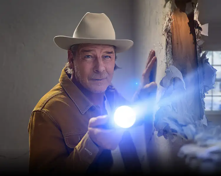 Ty Pennington inspecting hole in a wall with a flashlight