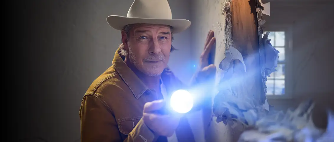 Ty Pennington inspecting hole in a wall with a flashlight
